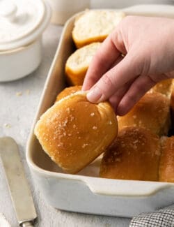 A hand lifts out a rhodes roll from a pan of rolls.