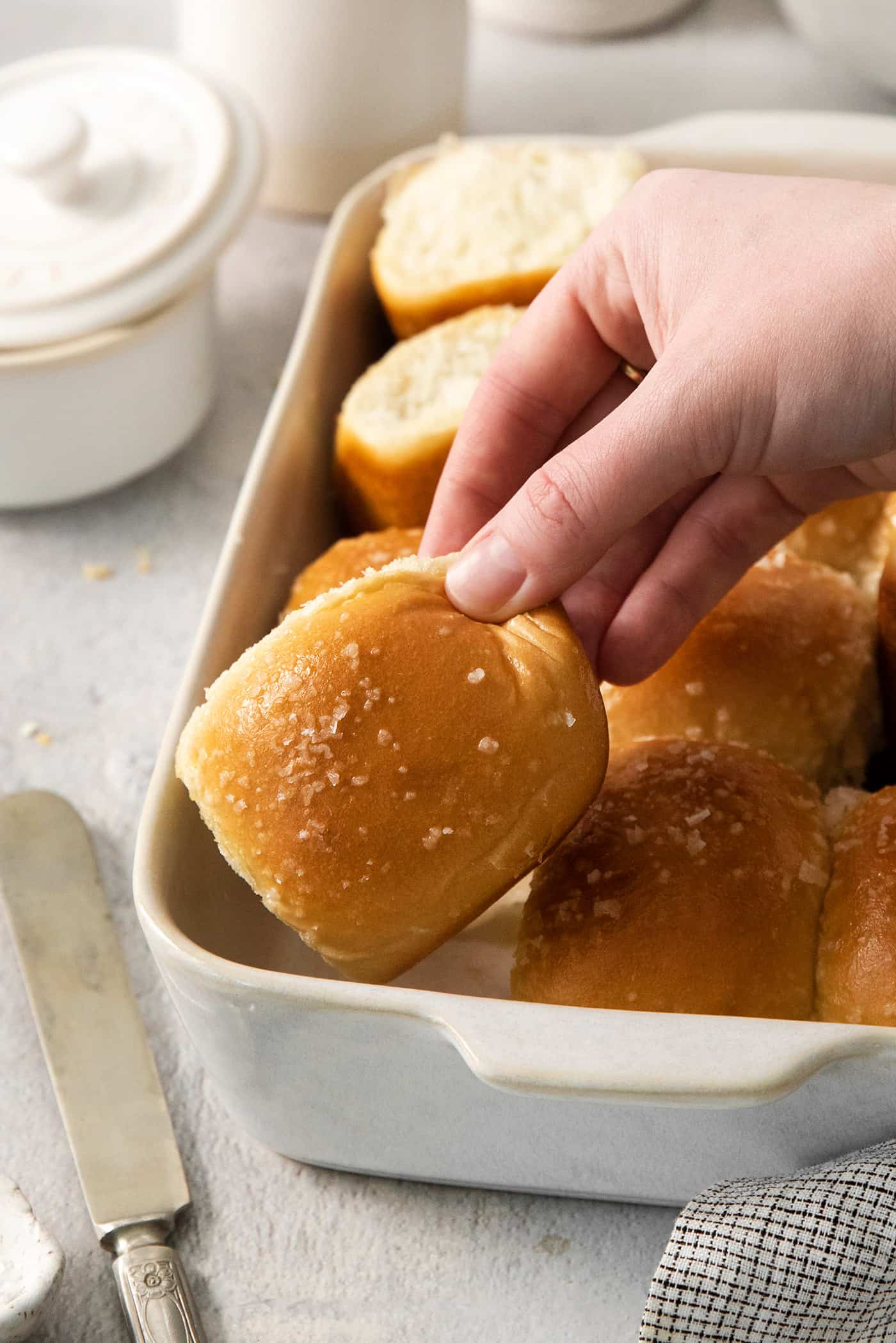 A hand lifts out a rhodes roll from a pan of rolls.