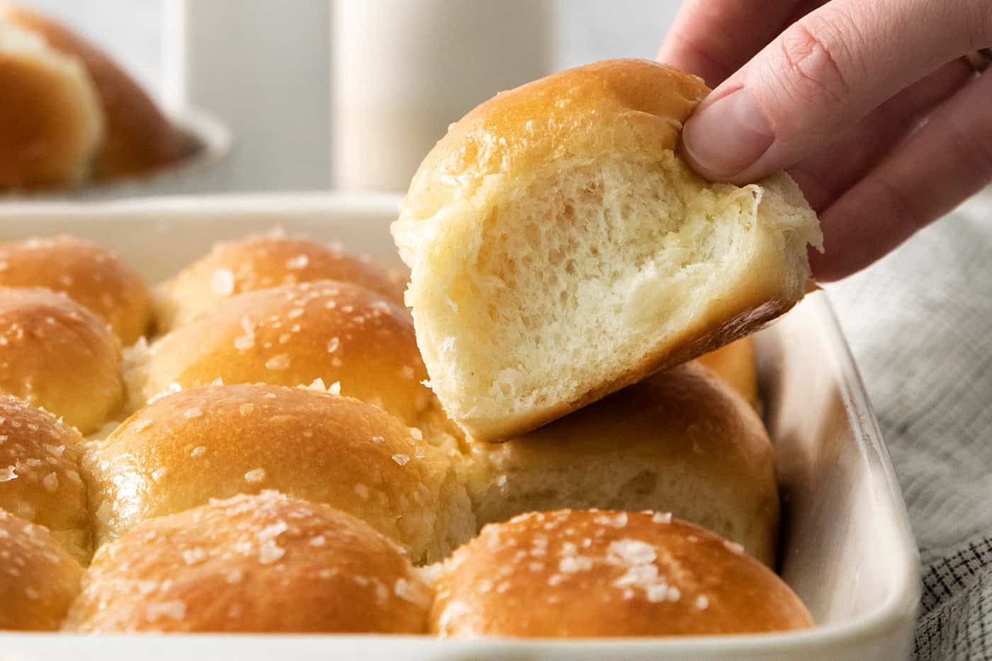 A hand holds a rhodes roll above a pan of rolls.