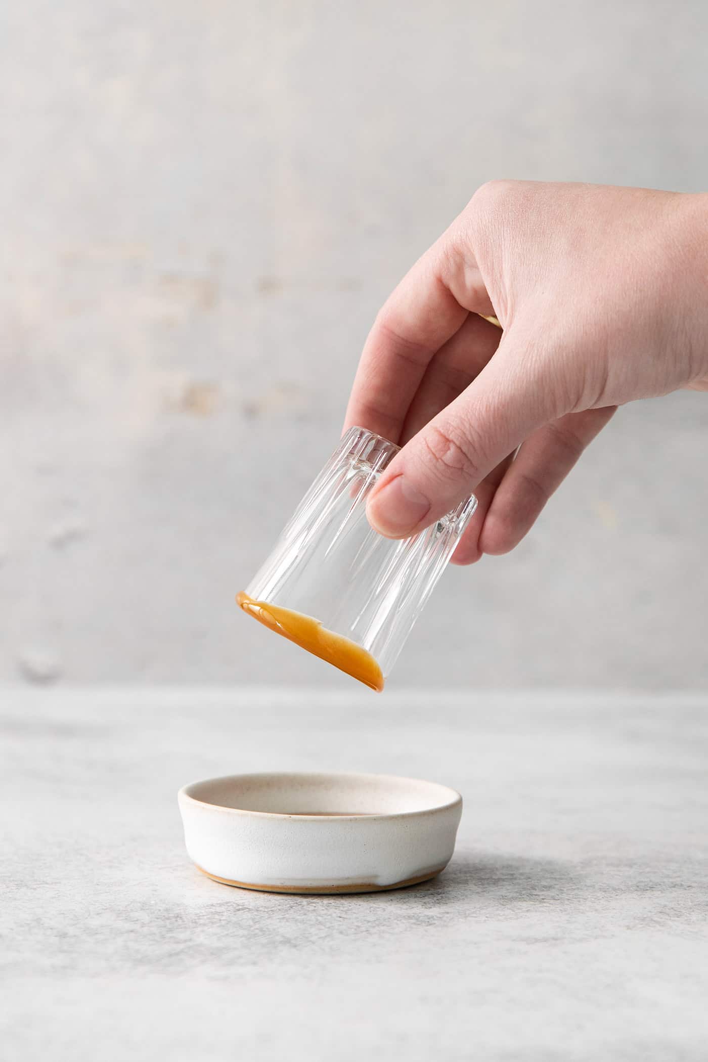 A hand dips a shot glass into a bowl of caramel sauce.