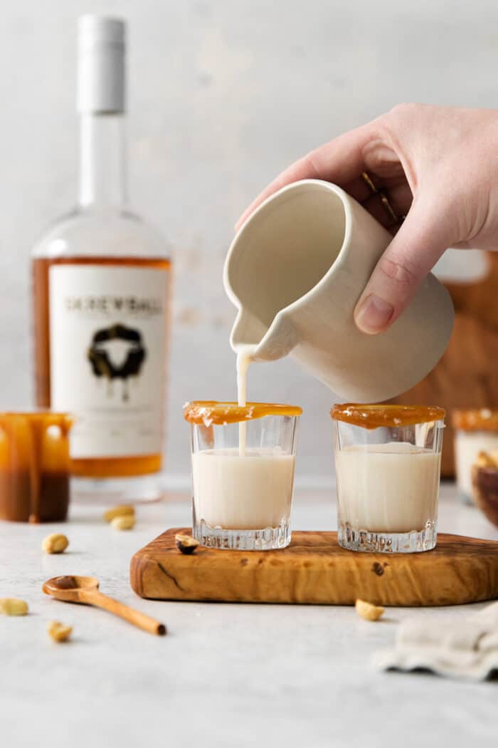 A hand holding a pitcher pours salted nut roll shots into shot glasses.