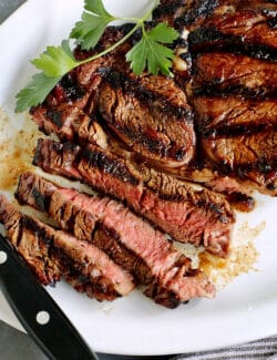 A platter of sliced sugar grilled steak with a knife resting on the edge of the plate.