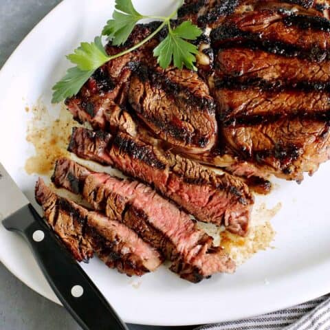 A platter of sliced sugar grilled steak with a knife resting on the edge of the plate.