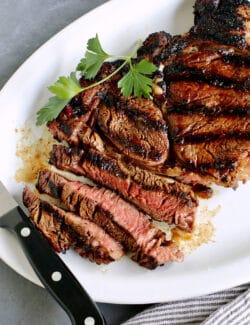 A platter of sliced sugar grilled steak with a knife resting on the edge of the plate.