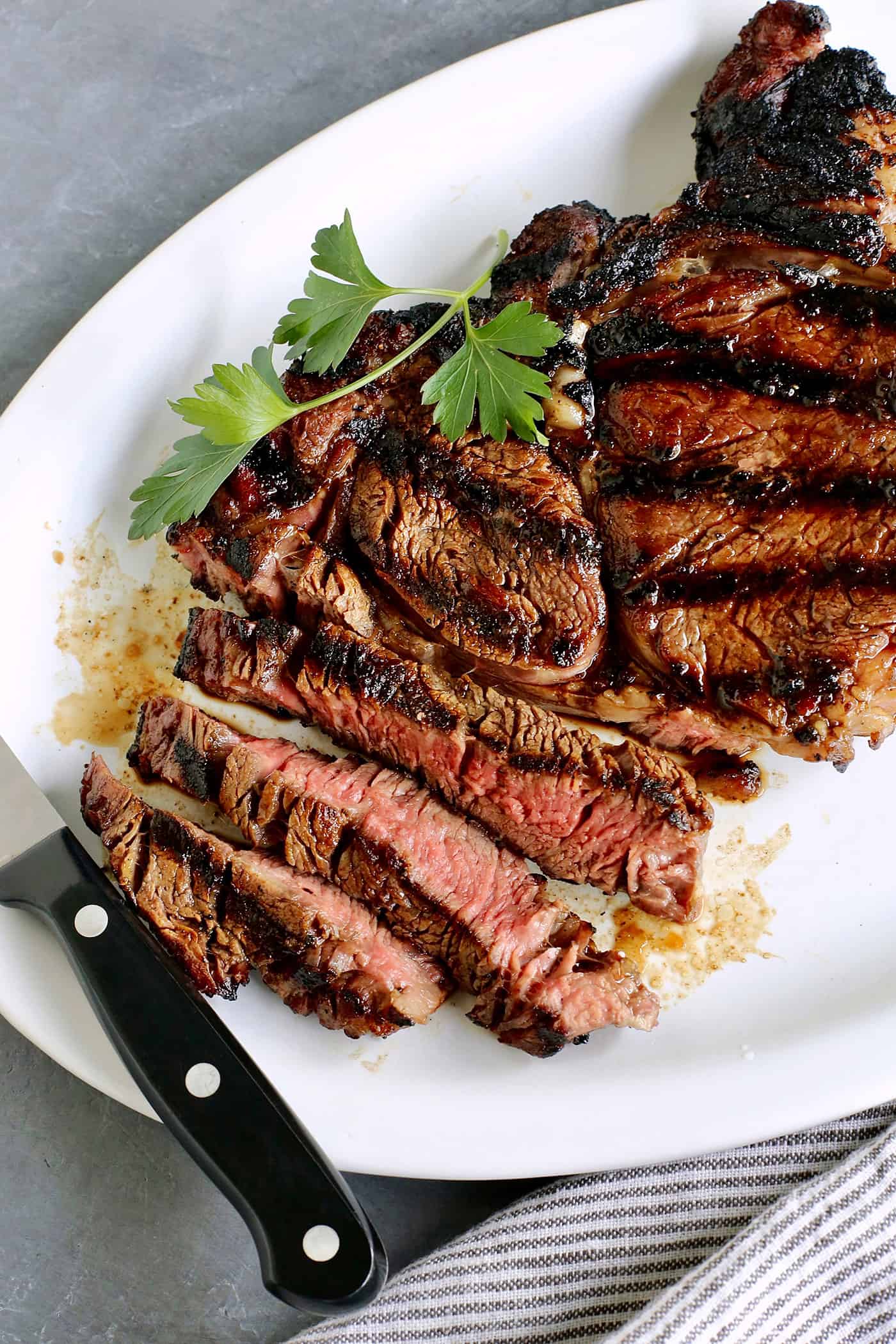 A platter of sliced sugar grilled steak with a knife resting on the edge of the plate.