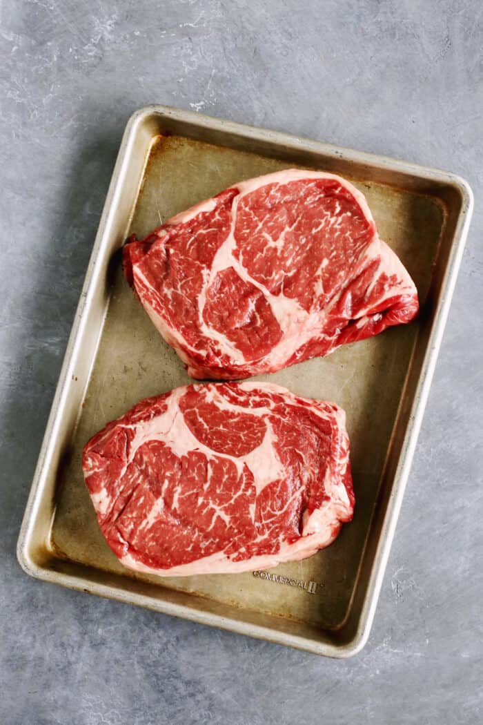 Two steaks are shown on a rimmed baking sheet.