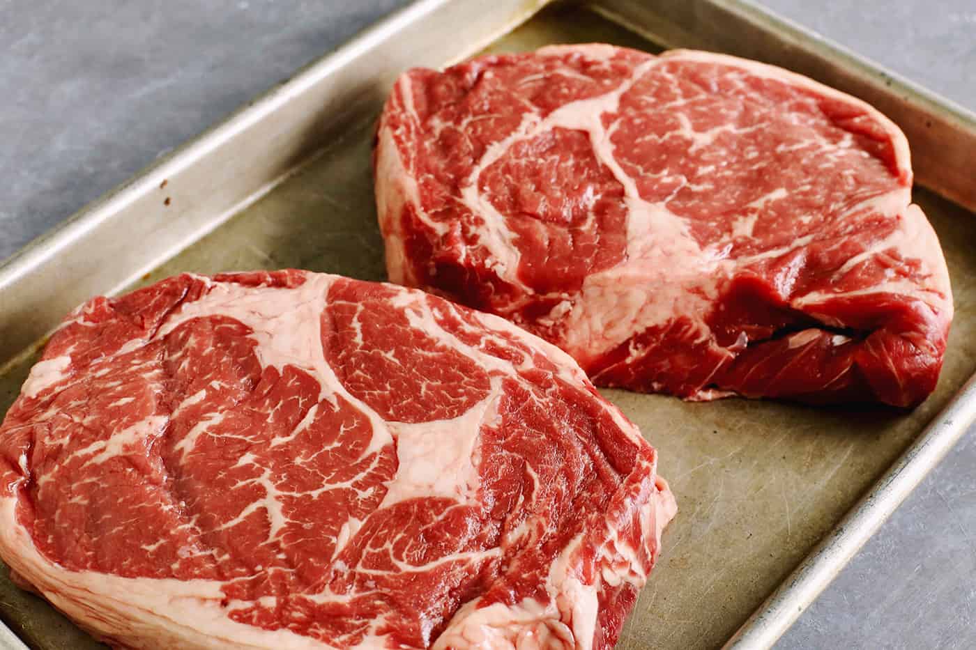 A close up shot of two steaks on a rimmed baking sheet.