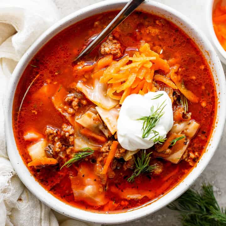 A bowl of unstuffed cabbage roll soup topped with carrot garnish and sour cream.