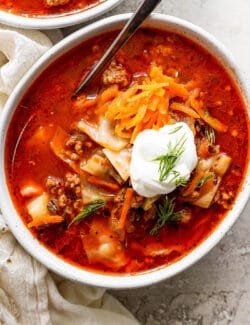 A bowl of unstuffed cabbage roll soup topped with carrot garnish and sour cream.