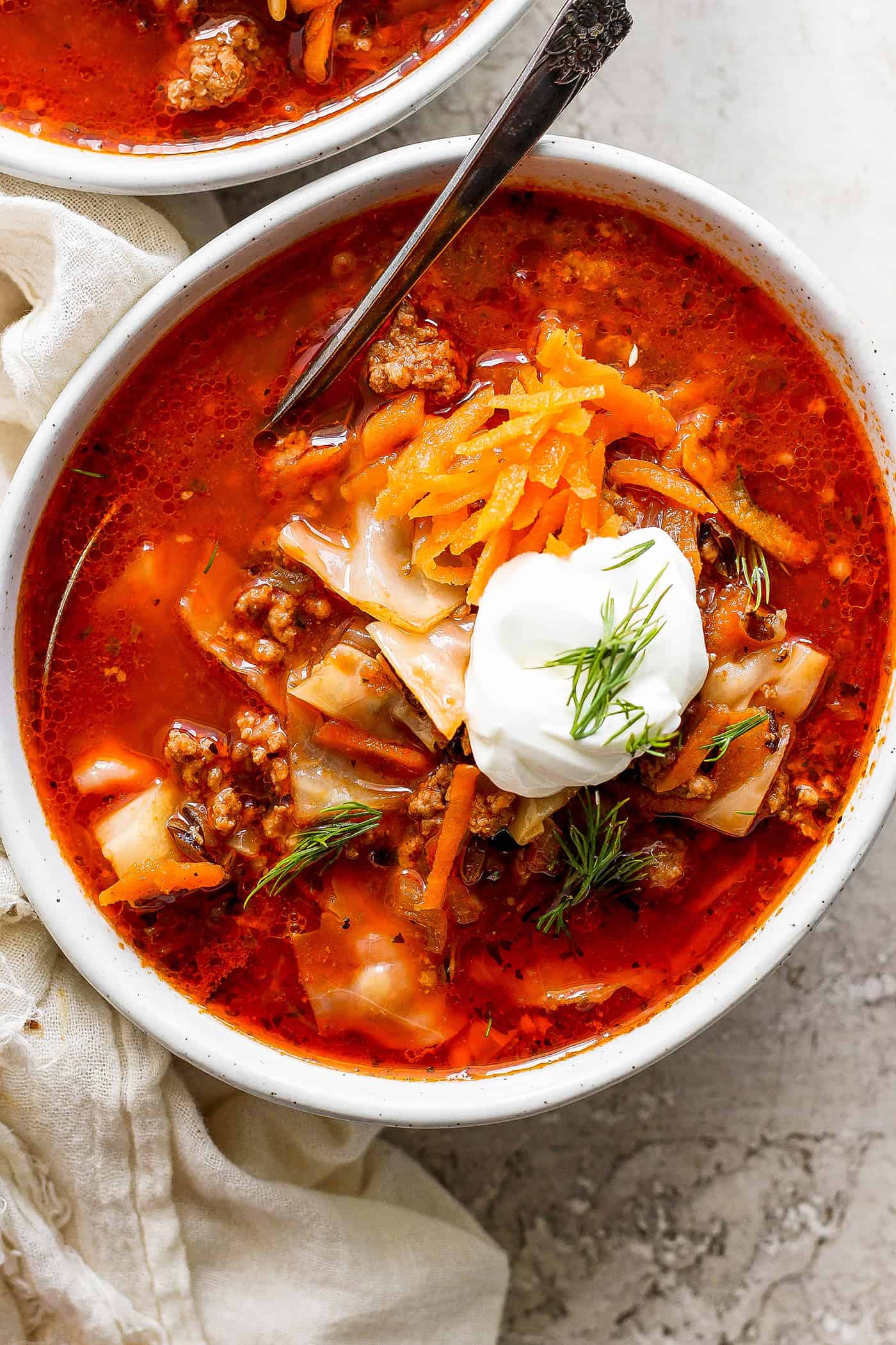 A bowl of unstuffed cabbage roll soup topped with carrot garnish and sour cream.