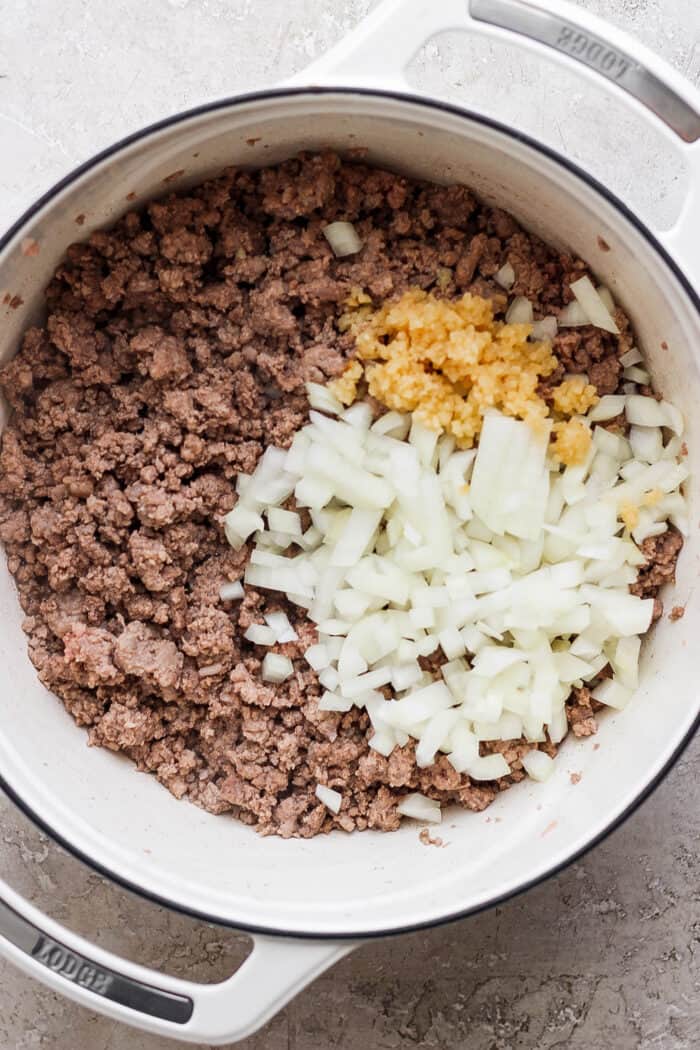 A pot of meat browns with onion and garlic on top.