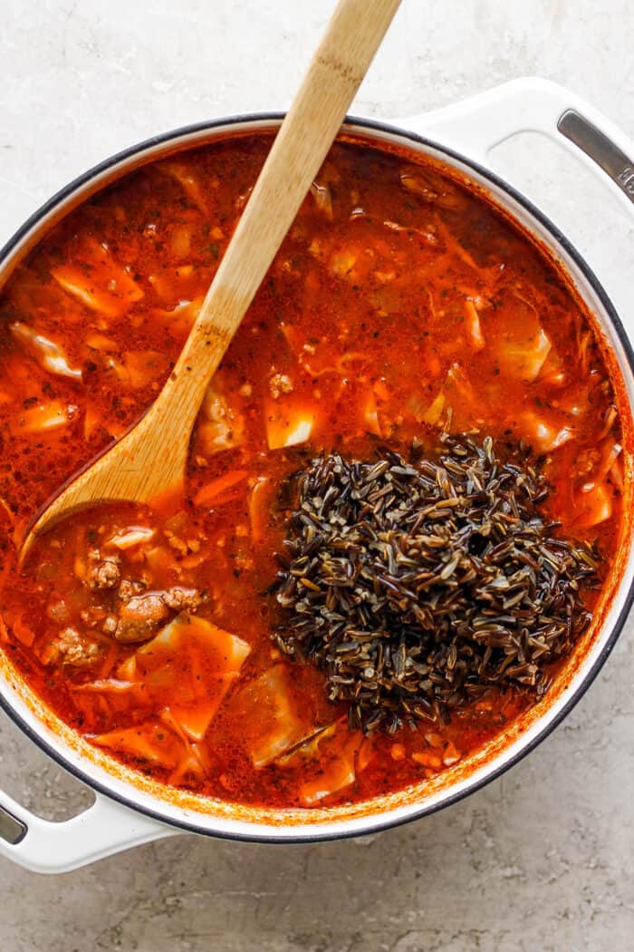 Wild rice is shown on top of a red pot of unstuffed cabbage roll soup.