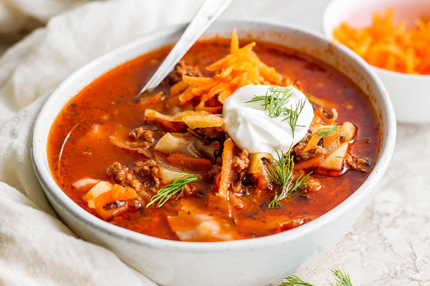 A bowl of unstuffed cabbage roll soup topped with carrot garnish and sour cream.