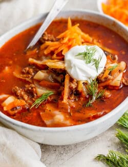 A bowl of unstuffed cabbage roll soup topped with carrot garnish and sour cream.