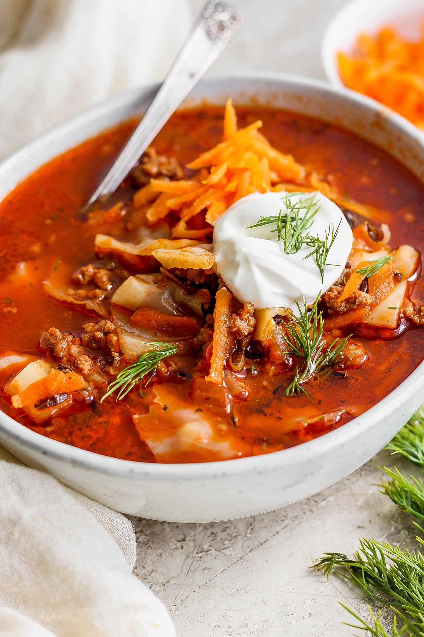 Hearty Unstuffed Cabbage Roll Soup takes everything you love about cabbage rolls and turns them into an easy soup! A bowl of unstuffed cabbage roll soup topped with carrot garnish and sour cream.