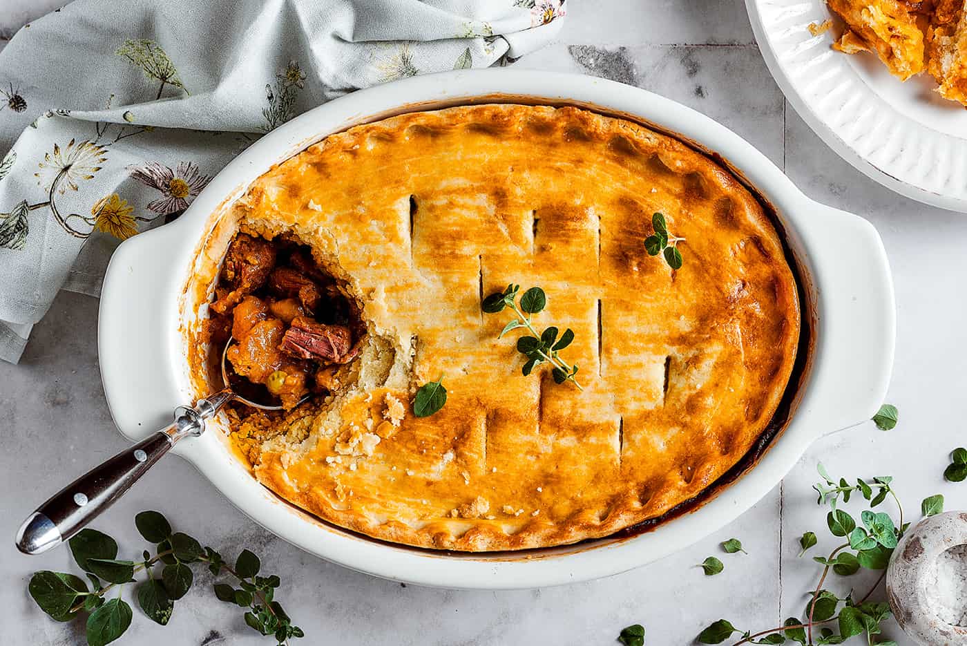 Overhead photos of an oval casserole dish of beef pot pie, with a spoon breaking into the top