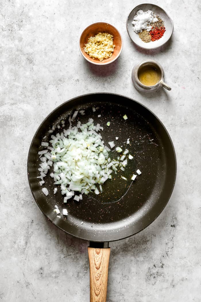 A chopped onion cooks in a black skillet.