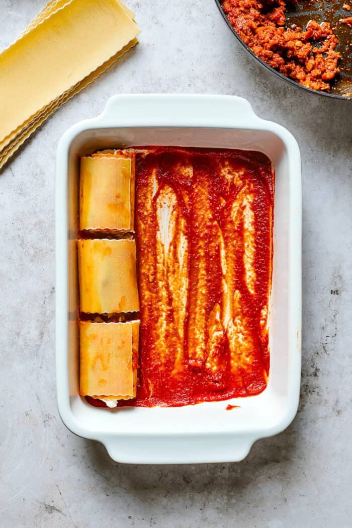 Three lasagna roll ups are shown on top of red sauce in a white baking dish.