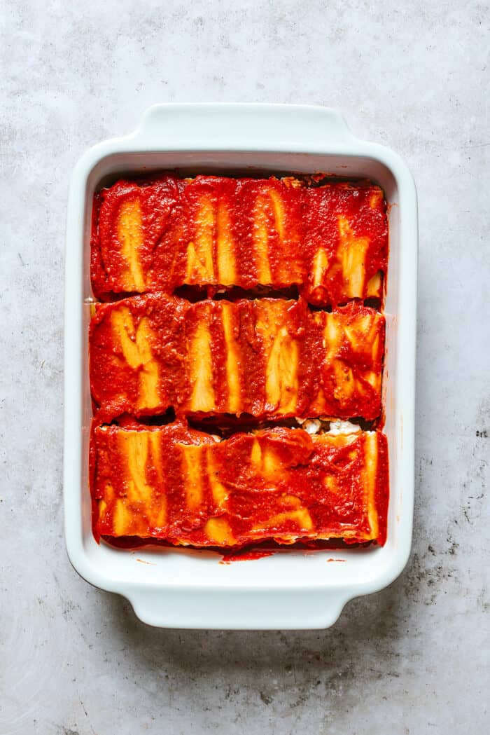 Lasagna roll ups are shown topped with red sauce in a white baking dish.