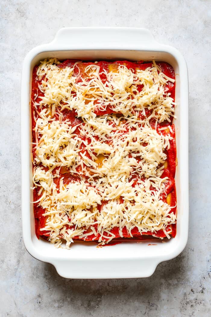 Shredded mozzarella cheese is scattered on top of a baking dish of lasagna roll ups.