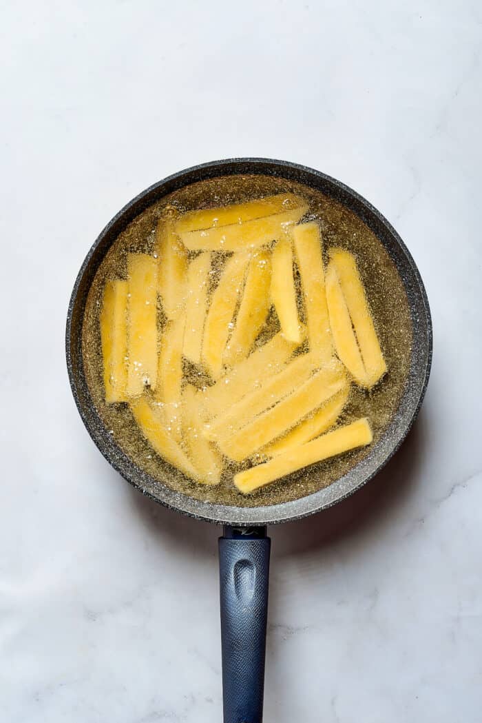 Sliced potatoes fry in oil in a frying pan.