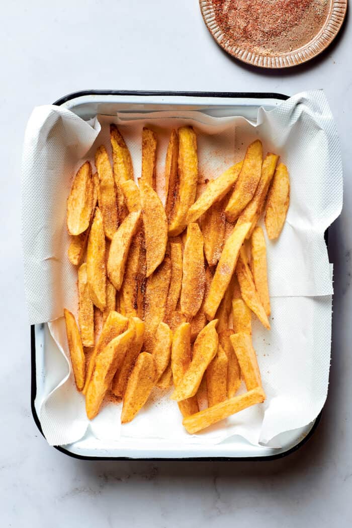 French fried potatoes drain on a paper towel-lined pan.