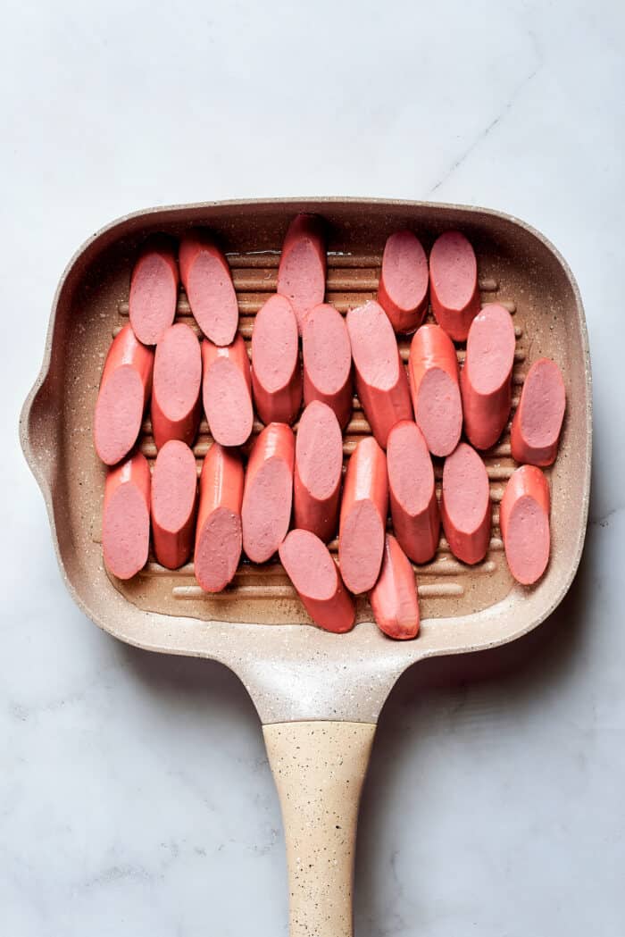 A cast iron grill pan holds thick slices of hot dogs.
