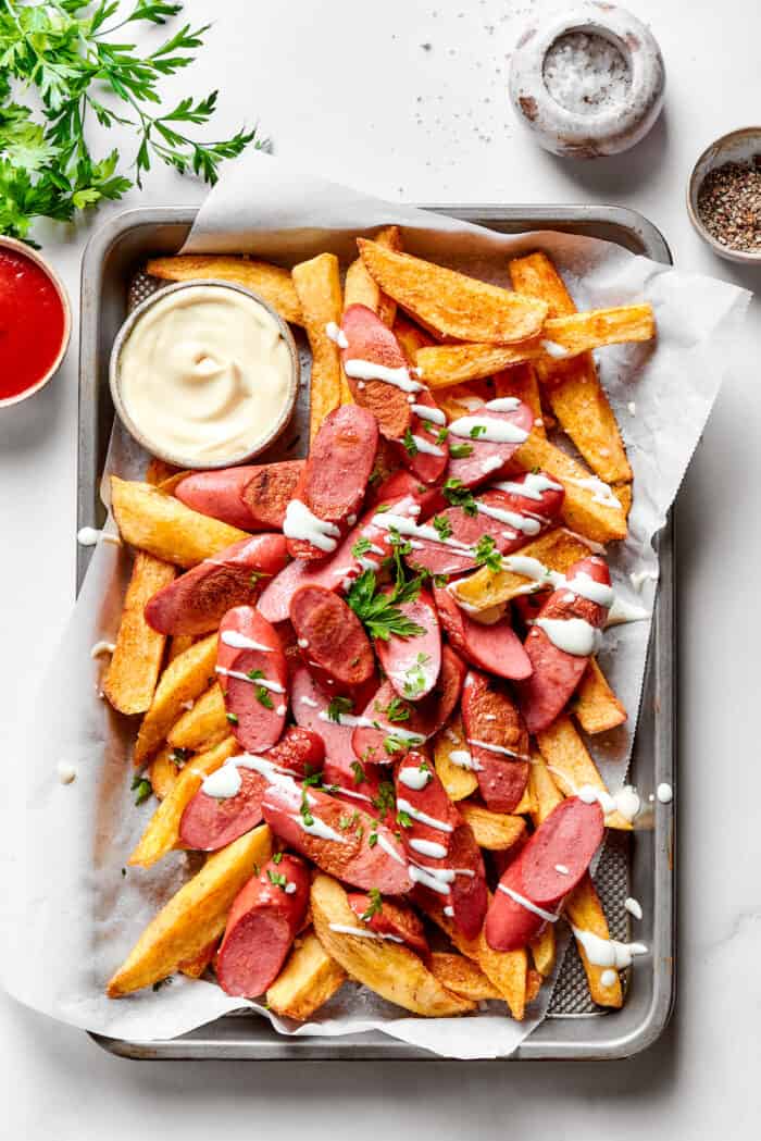 A tray of salchipapa, including homemade french fries, hot dogs, and a small bowl of mayonnaise.
