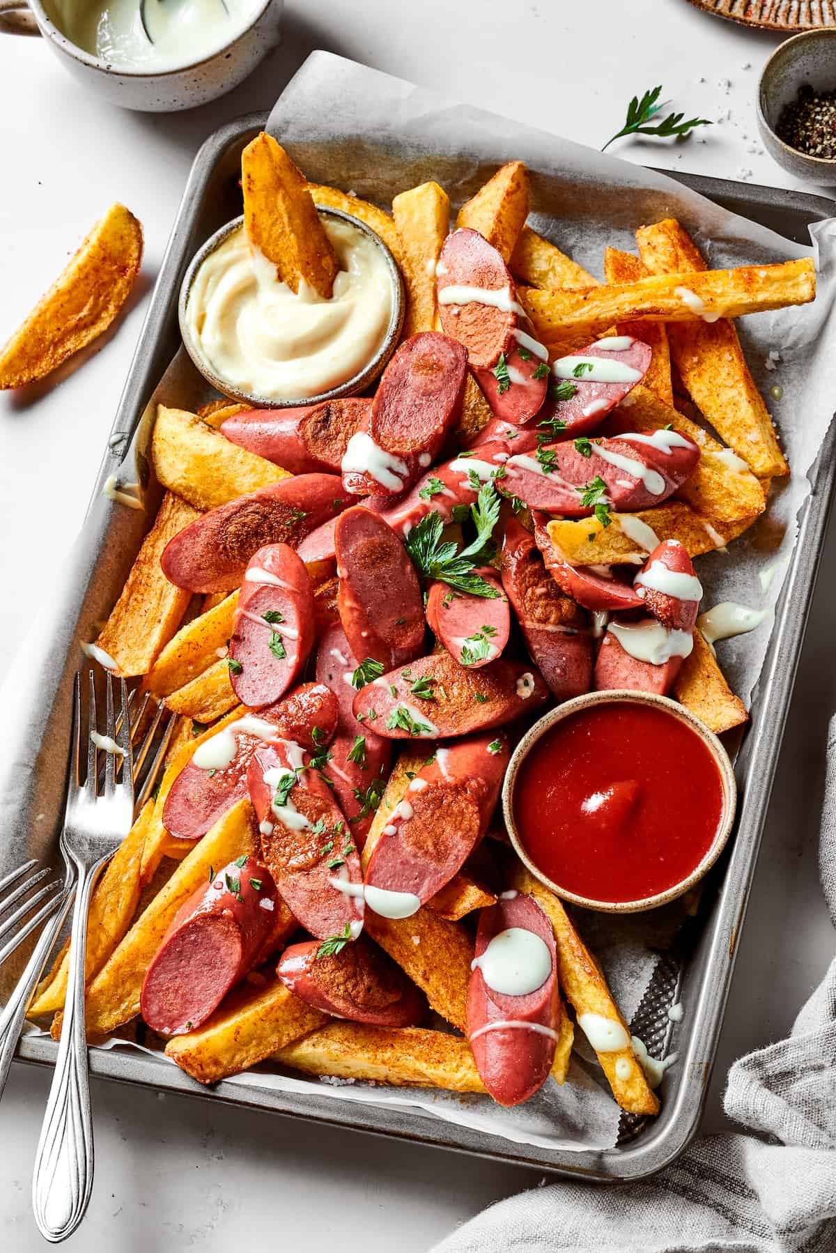 An angled tray of french fries and sliced hot dogs along with a small bowl of white mayonnaise and a small bowl of ketchup.