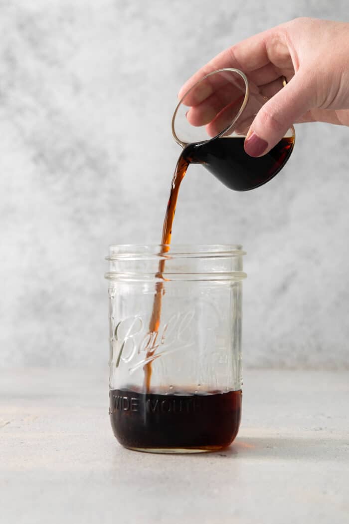 A hand pours creme de cacao into a jar of Brandy Alexander.