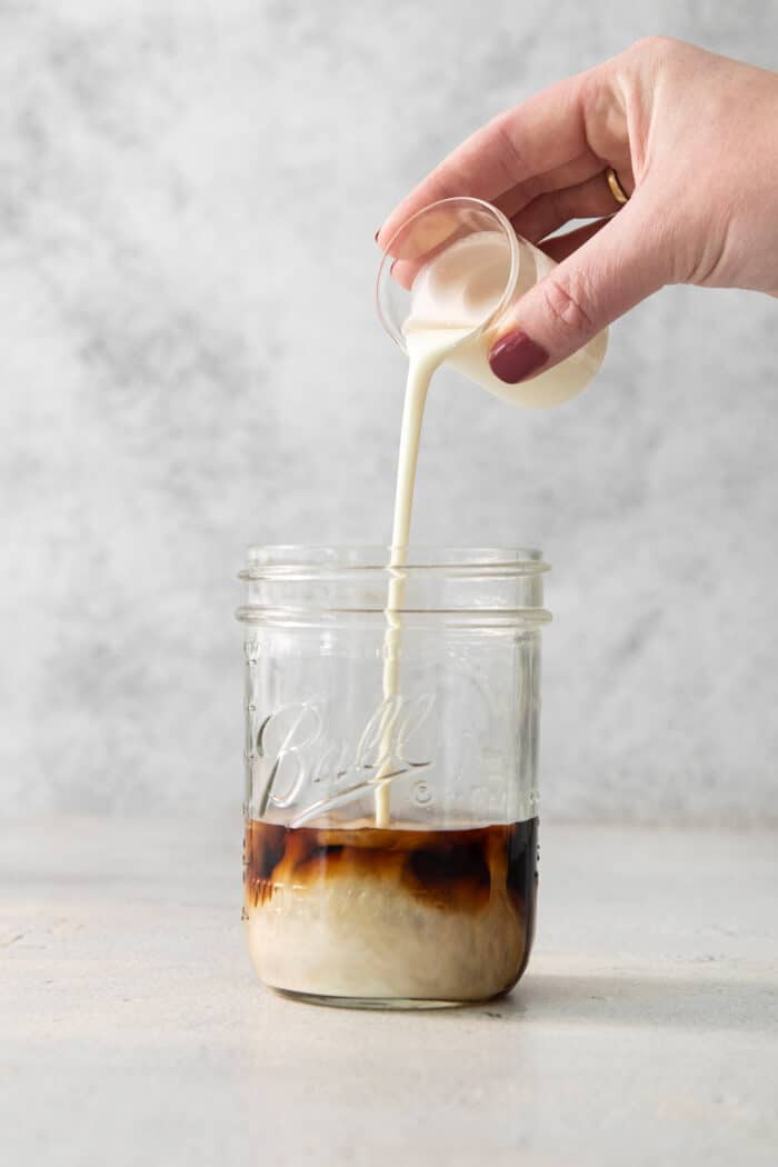 A hand pours cream into a jar of Brandy Alexander.