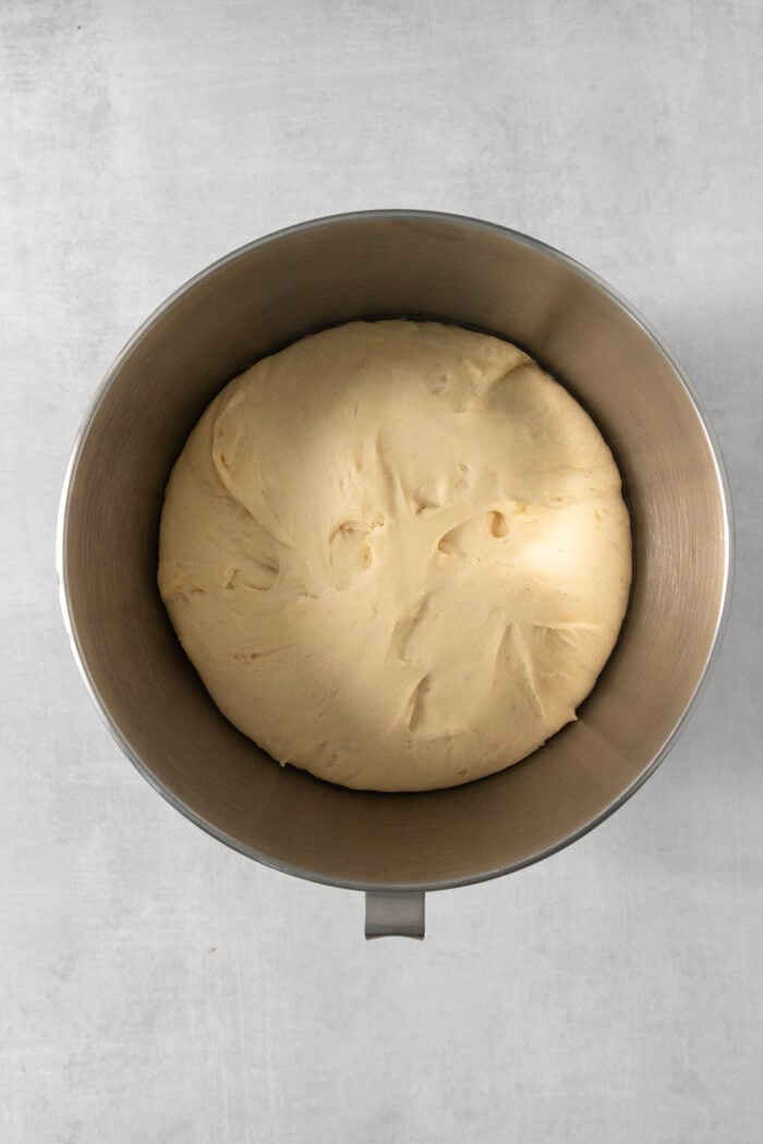 Proofed dough for caramel rolls in a silver bowl.