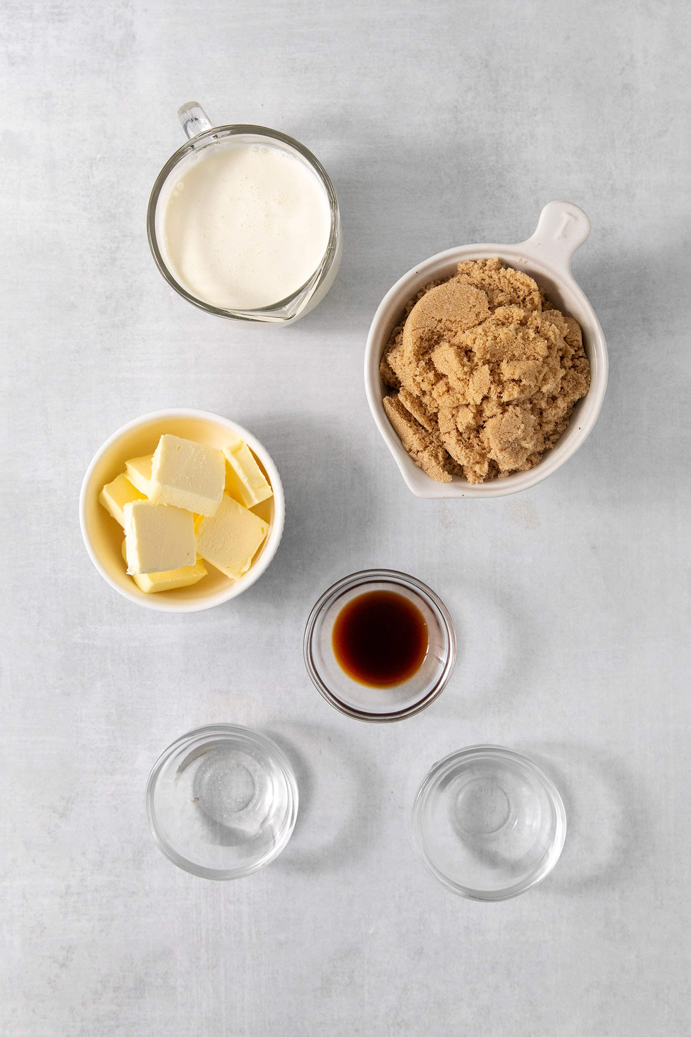 Ingredients for caramel sauce are shown portioned out in bowls: water, brown sugar, butter, vanilla, cream.