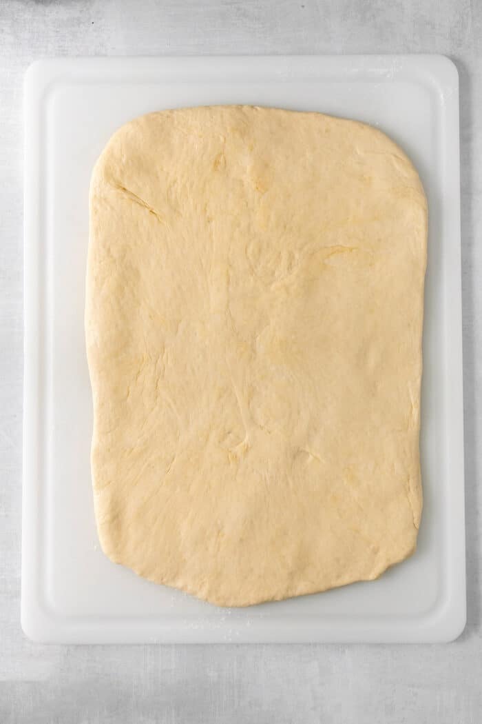 A rectangle of caramel rolls dough is stretched out on a white cutting board.