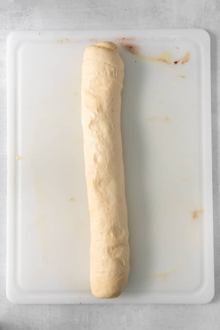 A log of filled caramel rolls dough on a white cutting board.