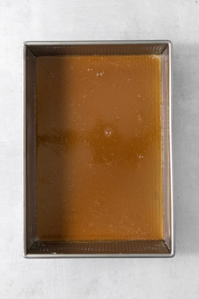 Caramel sauce is spread on the bottom of a rectangular metal baking dish.