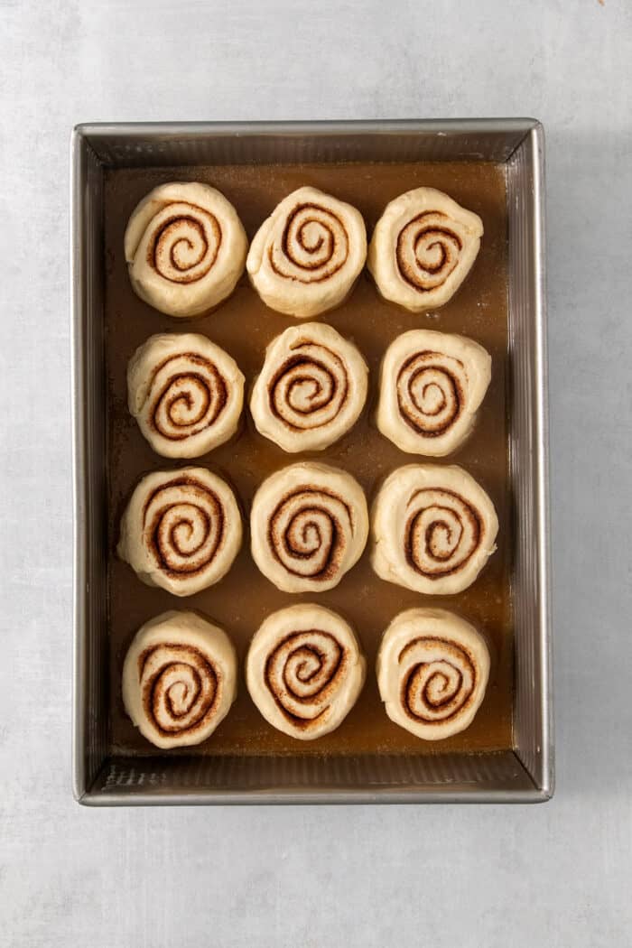 Twelve cut caramel rolls are shown on top of caramel sauce in a baking pan.
