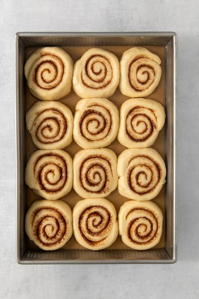Twelve proofed caramel rolls in a baking pan before being baked.