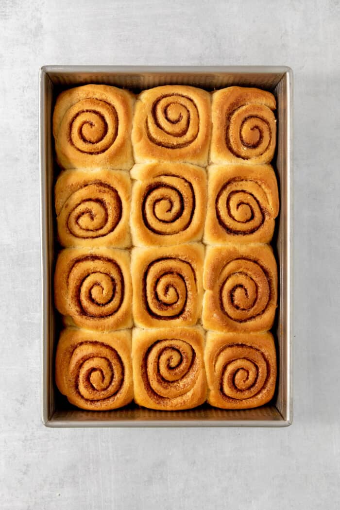 A rectangular baking dish holds 12 baked caramel rolls so that you can see the cinnamon inside.