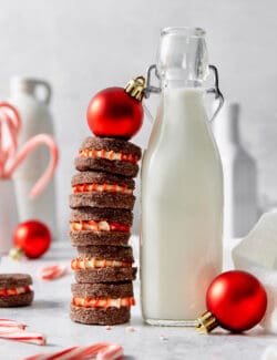 A tall stack of chocolate cream wafer cookies is topped with a red ornament and shown next to a jug of milk.