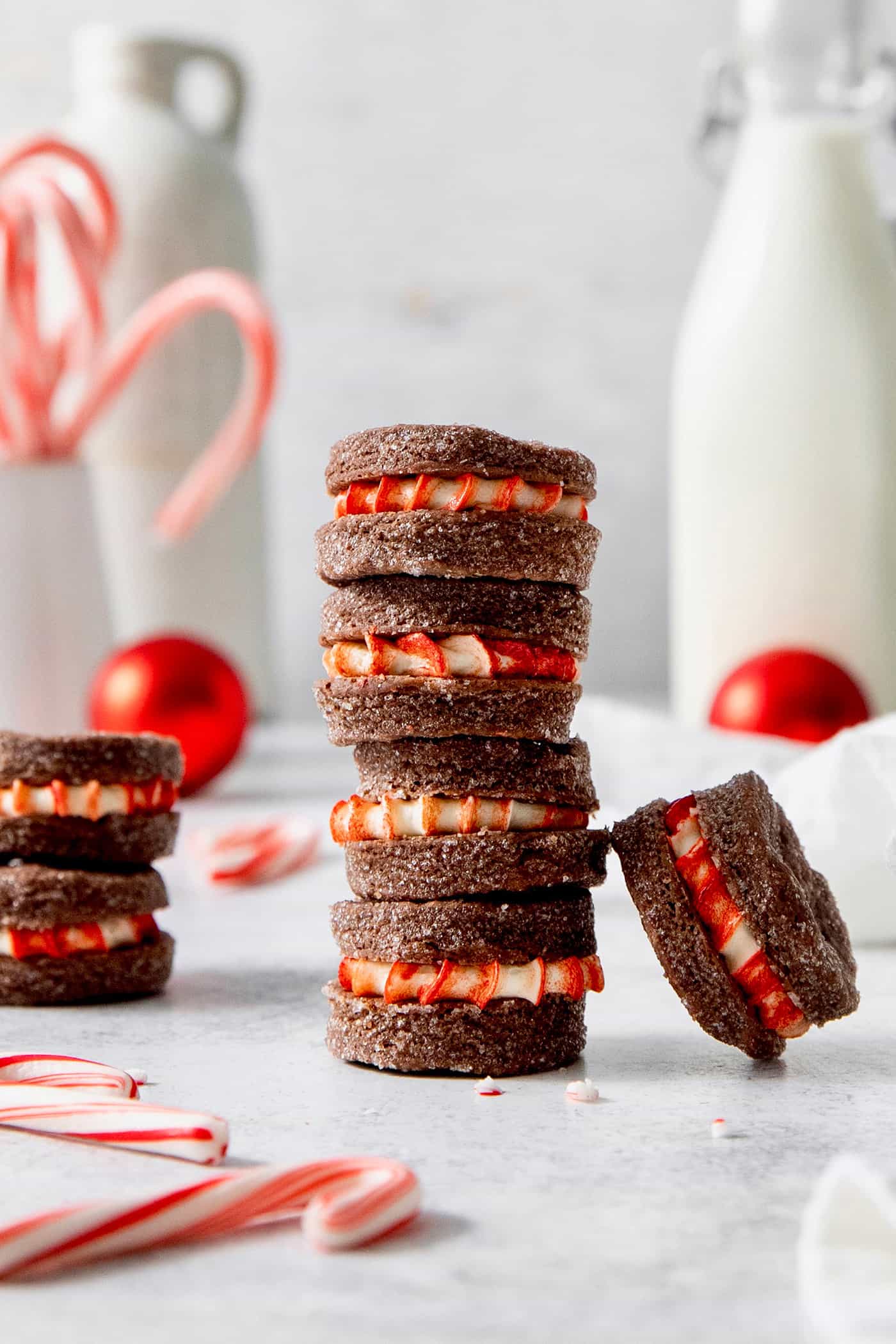 These Chocolate Cream Wafer Cookies feature buttery cocoa cookies that are soft, tender, and filled with a rich buttercream. A stack of three chocolate wafer cookies with peppermint filling and more scattered nearby.