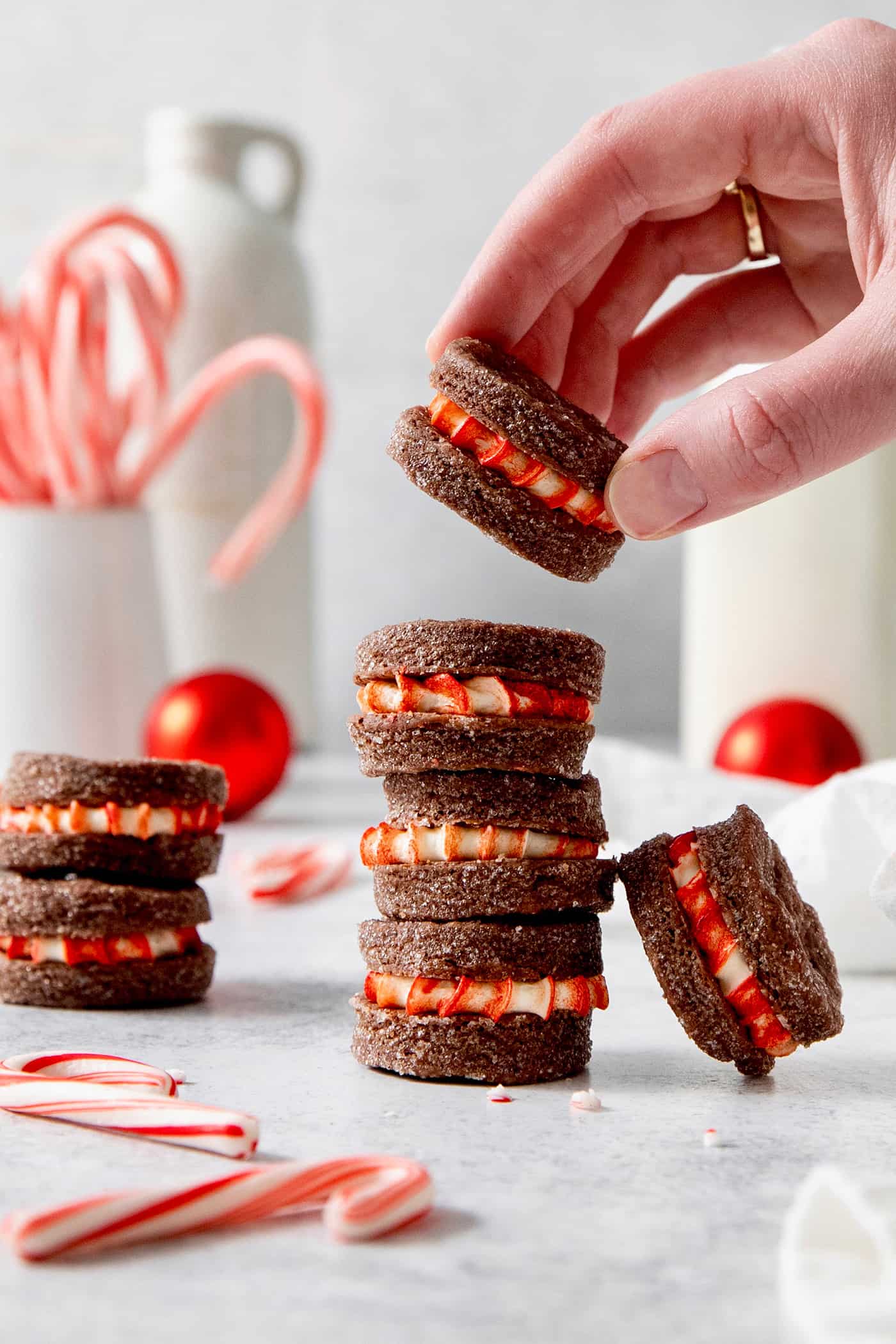 A hand picks up a chocolate cream wafer cookie from a stack of cookies, with candy canes seen in the background.