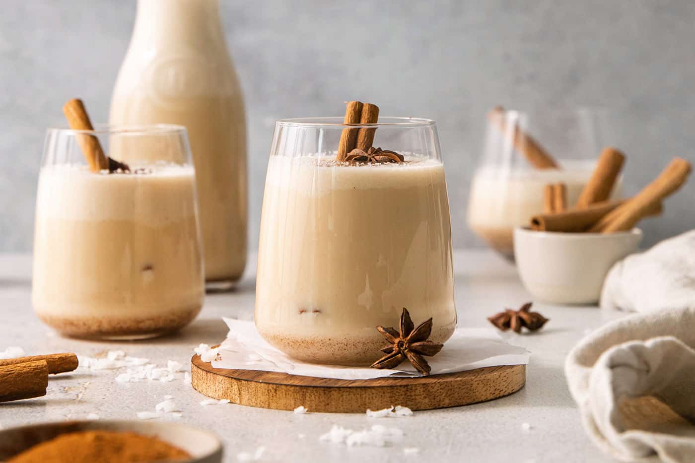 Glasses of coquito garnished with cinnamon sticks.