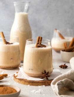 Glasses of coquito garnished with cinnamon sticks.