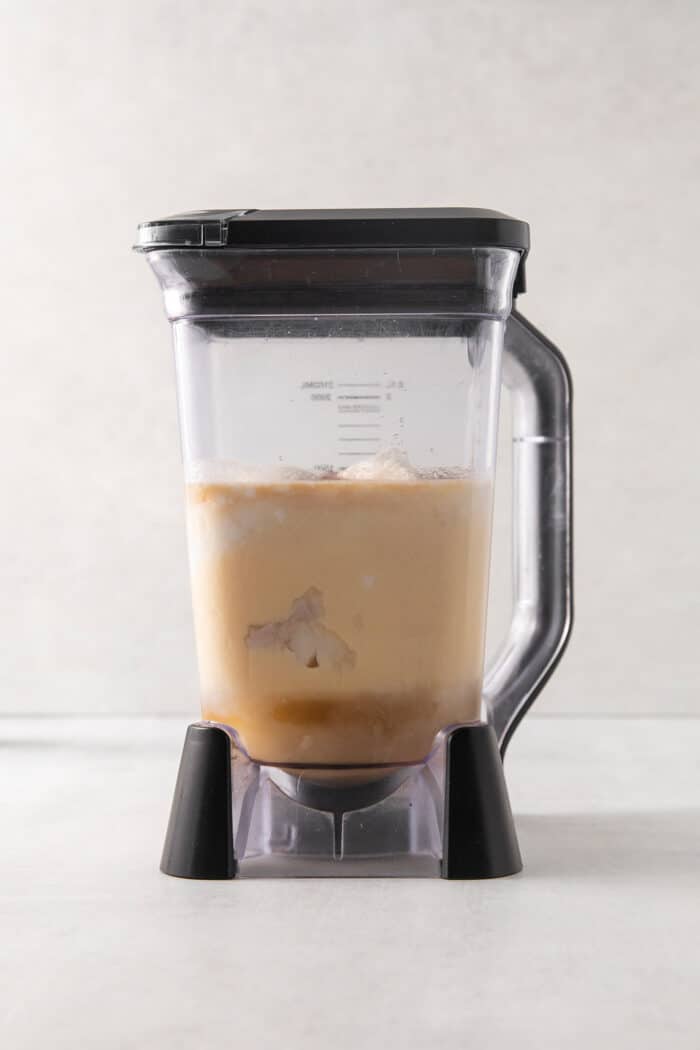 A blender with the top on full of coquito.