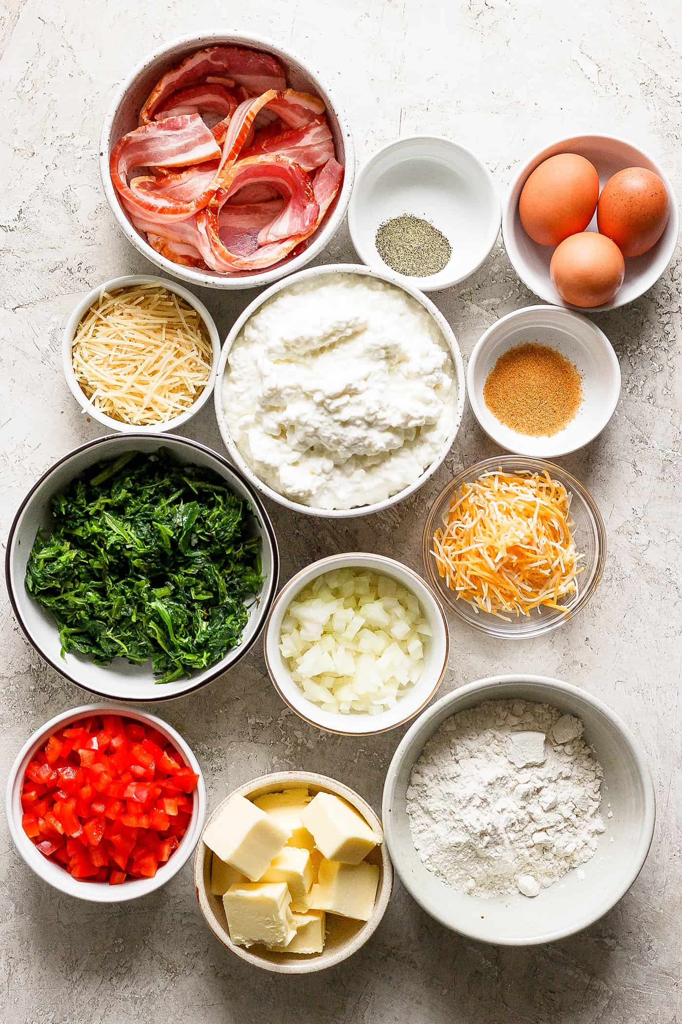 Ingredients for cottage cheese egg bake are shown portioned out: spinach, eggs, bacon, cheeses, flour, pepper, onion.