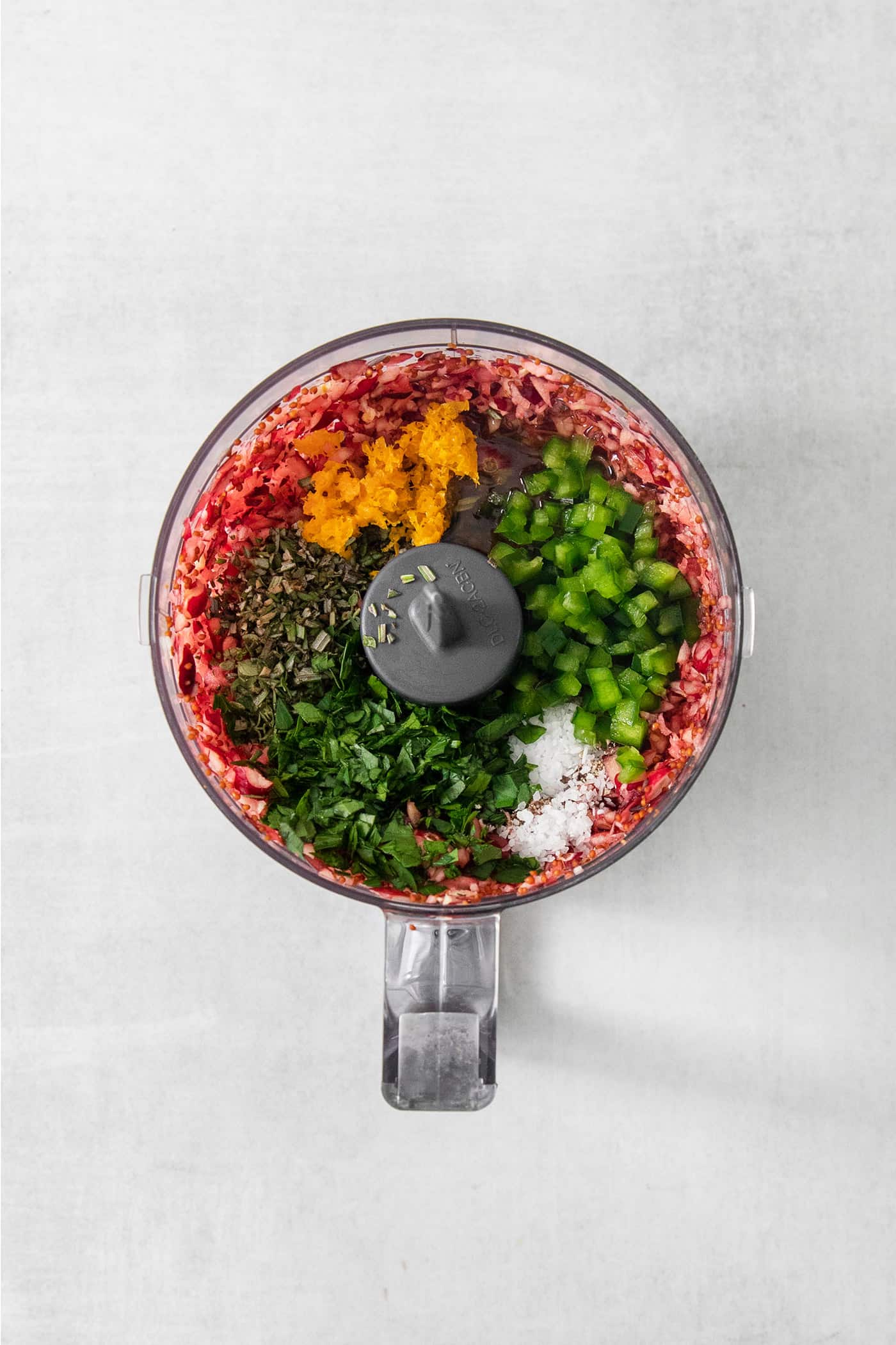 A food processor holds cranberries, jalapenos, herbs, and orange zest.