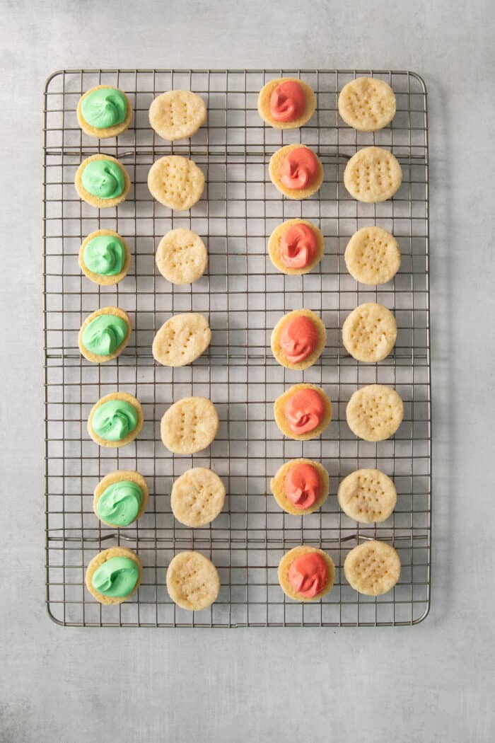 Colored filling is added to cream wafer cookies on a wire rack.