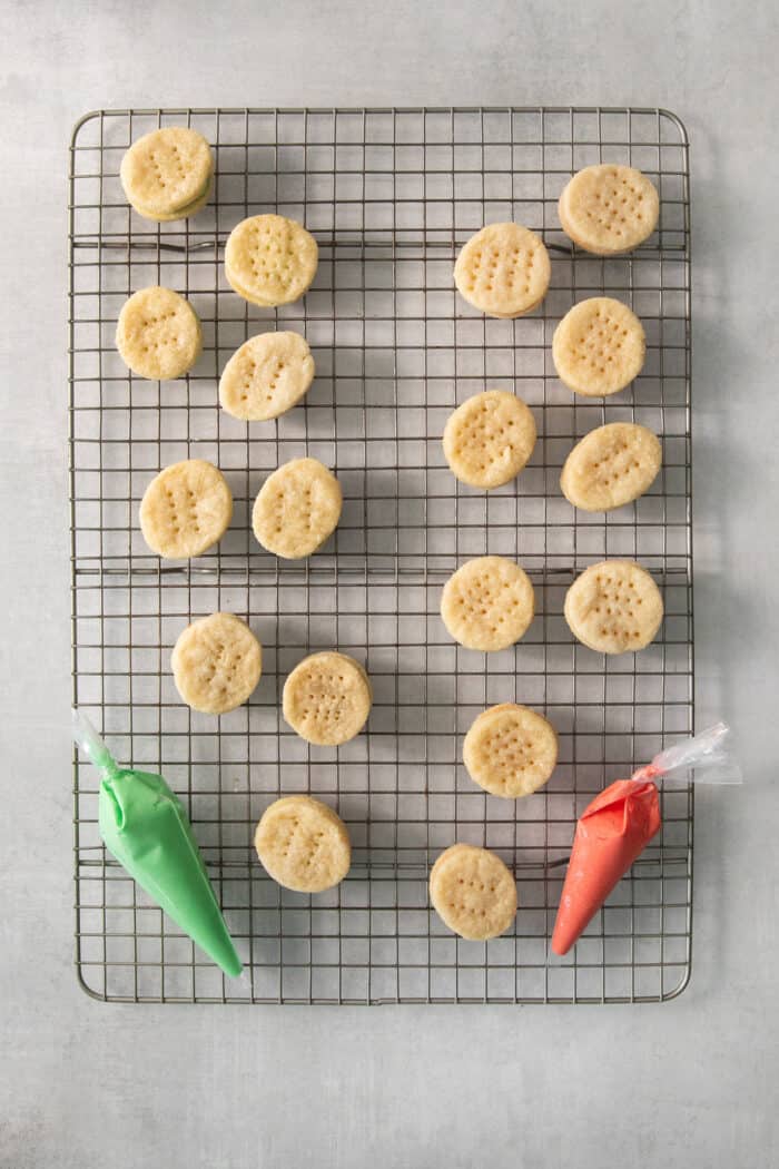 A wire rack of cream wafer cookies and bags of colored filling.