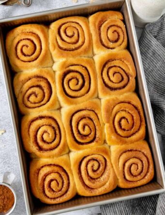 A pan of 12 caramel rolls is shown in a rectangular metal baking dish.